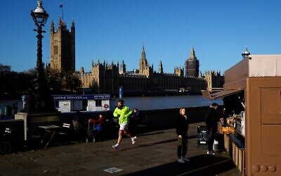 A jogger runs past the Palace of Westminster, comprising the House of Lords and the House of Commons, on the banks of the River Thames in London on November 22, 2021. (Niklas Halle'n/AFP)