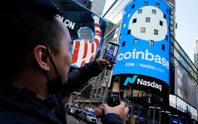 Coinbase employee Daniel Huynh holds a celebratory bottle of champagne as he photographs outside the Nasdaq MarketSite, in New York's Times Square, Wednesday, on April 14, 2021. (AP/Richard Drew) Coinbase employee Daniel Huynh holds a celebratory bottle of champagne as he photographs outside the Nasdaq MarketSite, in New York's Times Square, Wednesday, on April 14, 2021. (AP/Richard Drew)