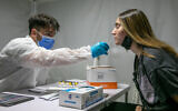 A Magen David Adom worker takes a swab sample from a woman at a coronavirus rapid testing station in the central city of Lod, October 17, 2021. (Yossi Aloni/Flash90)
