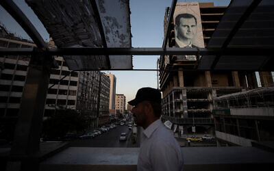Illustrative: A Syrian man walks over a bridge past a campaign poster of President Bashar Assad in the Syrian capital Damascus, on May 25, 2021. (AP Photo/Hassan Ammar)