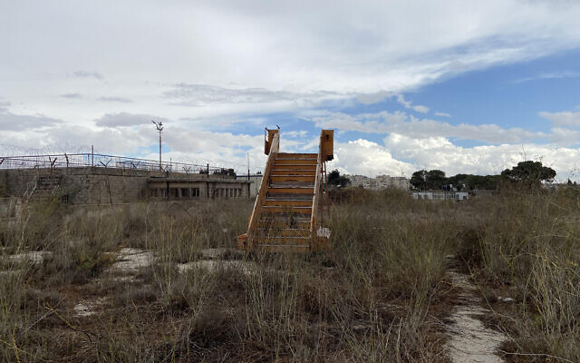 An "airstair" to nowhere rises from the weeds outside the abandoned terminal building of Jerusalem Airport at Atarot, November 2021. (David Horovitz / Times of Israel)