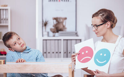 A counselor with posters of red and blue icons teaching an autistic child. (KatarzynaBialasiewicz  via iStock by Getty Images)