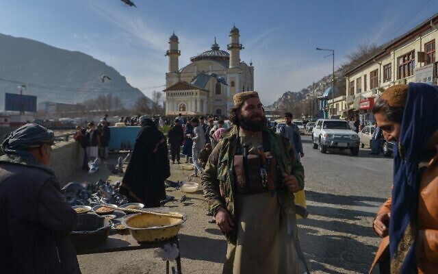 A member of the Taliban stands next to an Afghan hawker selling bird feed at a market area in Kabul on December 3, 2021. (Ahmad SAHEL ARMAN / AFP)