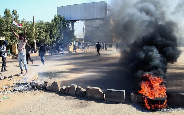 Sudanese demonstrators lift national flags as they block a road with bricks and burning tires during a rally in the capital Khartoum, on December 6, 2021. (AFP) Sudanese demonstrators lift national flags as they block a road with bricks and burning tires during a rally in the capital Khartoum, on December 6, 2021. (AFP)