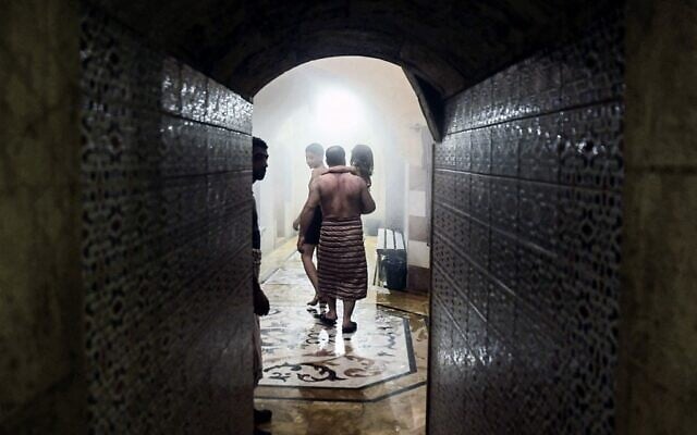 A man carries a child inside Hammam al-Qawas, a traditional Turkish bathhouse, in Syria's northern city of Aleppo on December 16, 2021. (Photo by AFP)