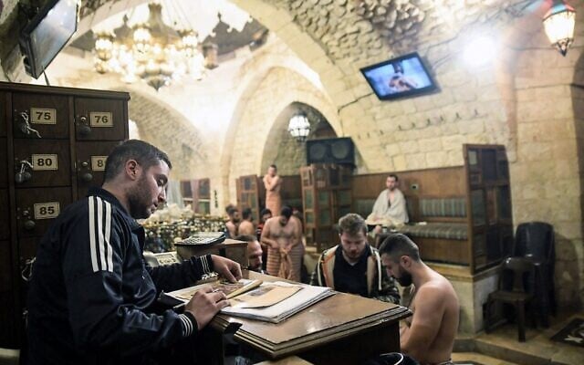 A worker checks the facility pamphlet at the entrance of Hammam al-Qawas, a traditional Turkish bathhouse, in Syria's northern city of Aleppo on December 16, 2021. (Photo by AFP)