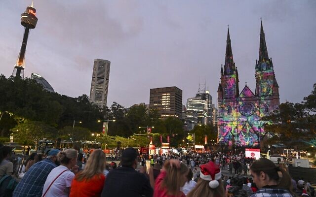 In this picture taken on December 23, 2021, people watch Christmas themed projections illuminated on St Mary's Cathedral in the central business district of Sydney. (Mohammad FAROOQ / AFP)