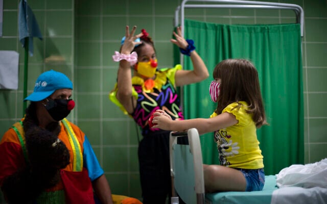 A girl is entertained by clowns as she waits in the control room after being injected with a dose of the Soberana-02 vaccine for COVID-19 in Havana, Cuba, August 24, 2021. (AP Photo/Ramon Espinosa)