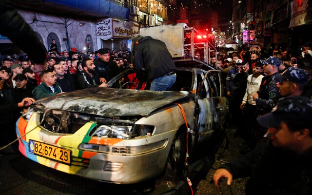 Palestinian police remove the remains of an Israeli car that was set on fire by a Palestinian crowd after two Israelis drove into the West Bank city of Ramallah, Wednesday, Dec. 1, 2021. (AP/Majdi Mohammed)
