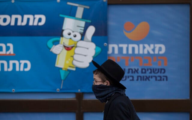 An ultra-Orthodox Jewish youth walks past a coronavirus vaccination center, in Jerusalem, Dec. 22, 2021 (AP Photo/Oded Balilty) An ultra-Orthodox Jewish youth walks past a coronavirus vaccination center, in Jerusalem, Dec. 22, 2021 (AP Photo/Oded Balilty)