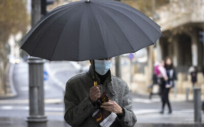 A man wearing a mask takes cover from the rain on Jaffa Road  in the city center of Jerusalem on December 21, 2021. (Olivier Fitoussi/Flash90)