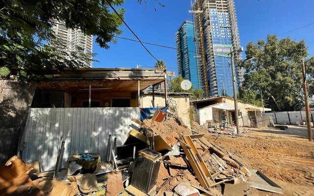 Piles of discarded household items outside Givat Amal homes, Park Bavli towers looming above them, on November 23, 2021. (Carrie Keller-Lynn/Times of Israel)