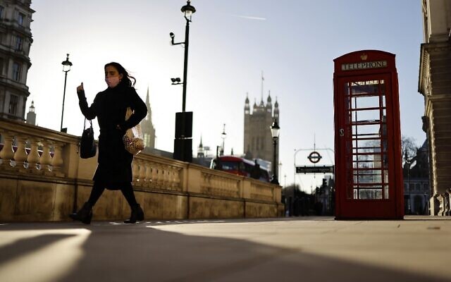 A woman wearing a face covering due to COVID-19 walks past a red telephone box on Whitehall, near the Houses of Parliament in central London, January 20, 2022. (Tolga Akmen/AFP) A woman wearing a face covering due to COVID-19 walks past a red telephone box on Whitehall, near the Houses of Parliament in central London, January 20, 2022. (Tolga Akmen/AFP)