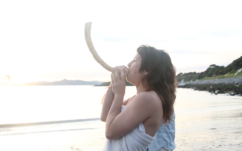 Rebecca Erev, co-founder of the Queer Mikveh Project, blows the shofar at the first QMP mikveh event at the Albany Bulb in Albany, California, in 2015. (Chani Bockwinkel/ via JTA)