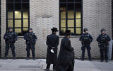 Illustrative: Jewish men pass New York City police guarding a Brooklyn synagogue prior to a funeral for Mosche Deutsch, a rabbinical student from Brooklyn who was killed in a shooting at a Jersey City, New Jersey kosher market, December 11, 2019. (AP Photo/Mark Lennihan, File)