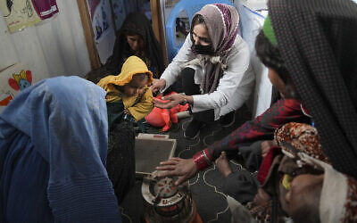 A nurse checks the weight of a child in a makeshift clinic organized by World Vision, at a settlement near Herat, Afghanistan, on December 16, 2021. (AP Photo/Mstyslav Chernov, File)