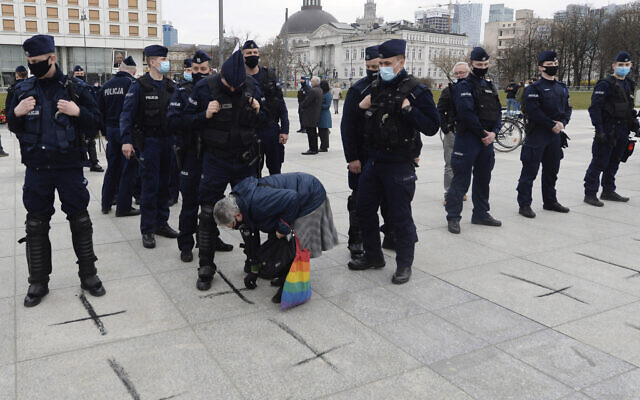 Police watch a woman paints black crosses on the pavement, for the victims of the COVID-19 pandemic in Pilsudski Square, Warsaw, Poland, on April 10, 2021. (AP Photo/Czarek Sokolowski) Police watch a woman paints black crosses on the pavement, for the victims of the COVID-19 pandemic in Pilsudski Square, Warsaw, Poland, on April 10, 2021. (AP Photo/Czarek Sokolowski)