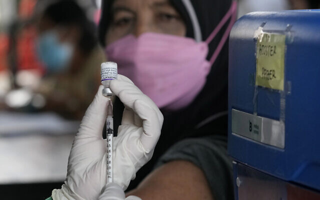A woman looks on, as a health worker prepares to administer a booster shot of Pfizer COVID-19 vaccine at a community health center in Jakarta, Indonesia, on January 12, 2022. (AP Photo/ Dita Alangkara) A woman looks on, as a health worker prepares to administer a booster shot of Pfizer COVID-19 vaccine at a community health center in Jakarta, Indonesia, on January 12, 2022. (AP Photo/ Dita Alangkara)