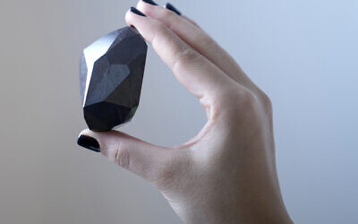 An employee of Sotheby's Dubai presents a 555.55 carat black diamond, 'The Enigma,' to be auctioned at Sotheby's Dubai gallery, in Dubai, United Arab Emirates, January 17, 2022. (AP Photo/ Kamran Jebreili)
