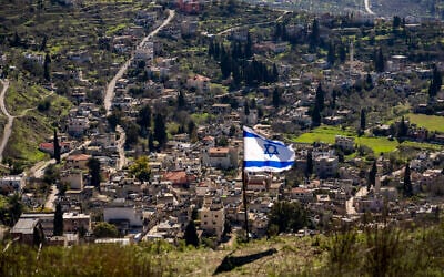 The Palestinian village of Burqa is seen as an Israeli flag is placed in the Jewish West Bank outpost of Homesh, January 17, 2022. (AP/Ariel Schalit)