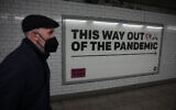 A man wearing a face mask to curb the spread of coronavirus walks past a health campaign poster from the One NGO, in an underpass leading to Westminster underground train station, in London, on January 27, 2022. (AP Photo/Matt Dunham)
