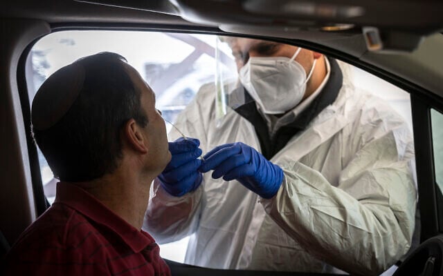 A Magen David Adom worker takes a swab sample from a man at a drive-thru testing complex in Jerusalem on January 17, 2022. (Olivier Fitoussi/Flash90) A Magen David Adom worker takes a swab sample from a man at a drive-thru testing complex in Jerusalem on January 17, 2022. (Olivier Fitoussi/Flash90)