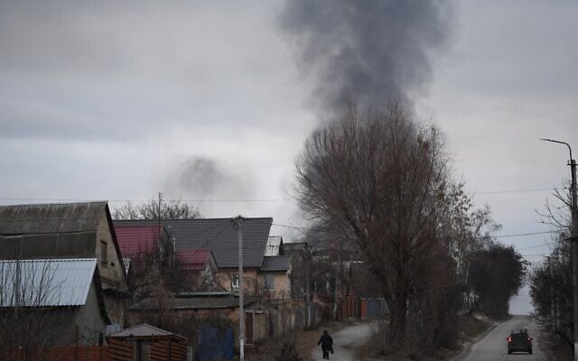 A local resident walks in a street as smoke rises near the town of Hostomel and the Antonov Airport, in northwest Kyiv on February 24, 2022. (Daniel LEAL / AFP)