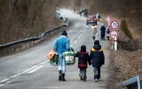 A woman with two children and carrying bags walk on a street to leave Ukraine after crossing the Slovak-Ukrainian border in Ubla, eastern Slovakia, close to the Ukrainian city of Welykyj Beresnyj, on February 25, 2022 (PETER LAZAR / AFP)