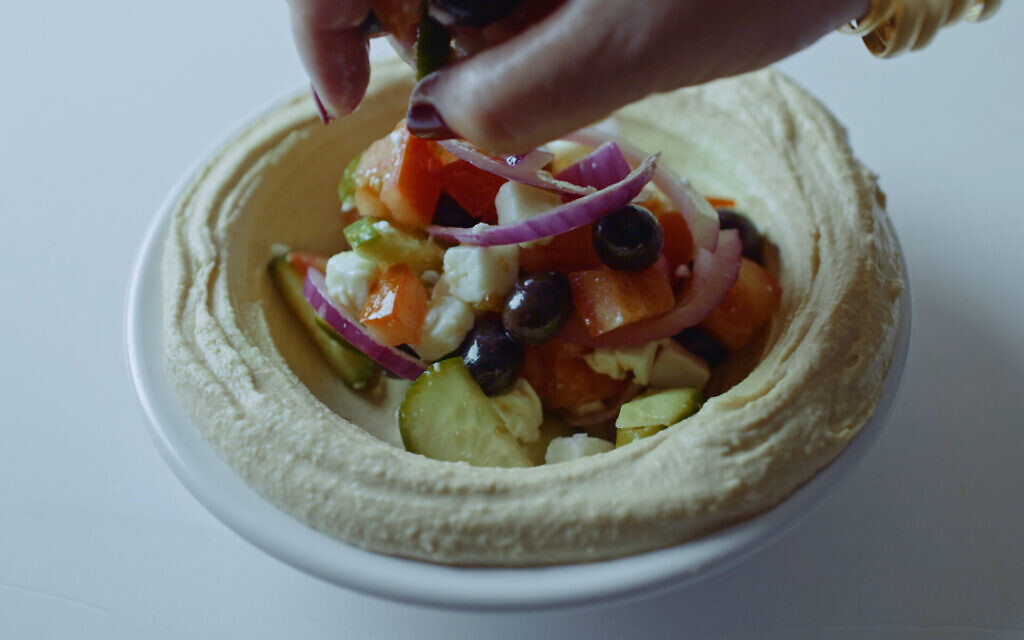 Hummus topped with Greek salad is prepared for an Israeli-Arab food festival in the documentary "Breaking Bread." (Cohen Media Group via JTA) Hummus topped with Greek salad is prepared for an Israeli-Arab food festival in the documentary "Breaking Bread." (Cohen Media Group via JTA)
