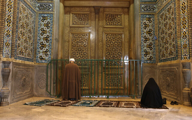 A cleric and a woman pray behind a closed door of Masoume shrine in the city of Qom, some 80 miles (125 kilometers) south of the capital Tehran, Iran, Monday, March 16, 2020. (AP)