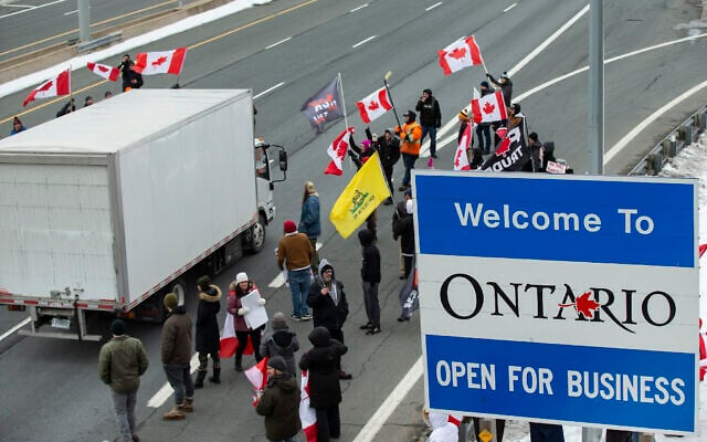 A truck passes Ontario Provincial Police officers and demonstrators in opposition to COVID-19 mandates on the Toronto-bound QEW highway after crossing the Peace Bridge in Fort Erie, Ontario on Feb. 12, 2022. (Aaron Lynett /The Canadian Press via AP)