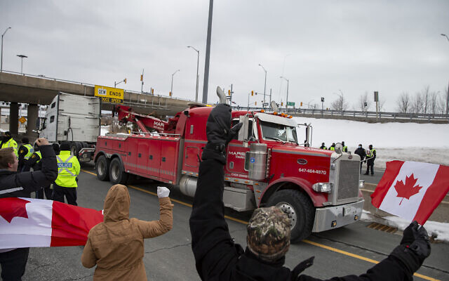 A truck passes Ontario Provincial Police officers and demonstrators in opposition to COVID-19 mandates on the Toronto-bound QEW highway after crossing the Peace Bridge in Fort Erie, Ontario, Feb.  12, 2022. The demonstrations at the Ambassador Bridge, downtown Ottawa and elsewhere have targeted vaccine mandates and other coronavirus restrictions and vented fury toward Prime Minister Justin Trudeau, who has called the protesters a “fringe” of Canadian society. (Aaron Lynett /The Canadian Press via AP)