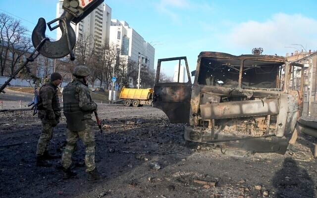 Ukrainian soldiers stand next to a burnt military truck, in a street in Kyiv, Ukraine, Feb. 26, 2022. (Efrem Lukatsky/AP)