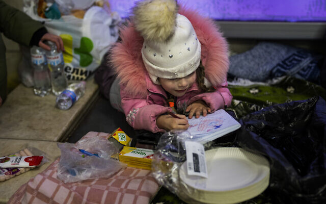 A girl paints on a notebook next to her mother as they shelter in the Kyiv subway, using it as a bomb shelter, Ukraine, on February 26, 2022. (AP Photo/Emilio Morenatti)