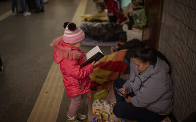 A girl looks at a notebook next to her mother as they stand in the Kyiv subway, using it as a bomb shelter, in Ukraine, on February 26, 2022. (AP Photo/Emilio Morenatti)
