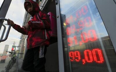 A food delivery man leaves an exchange office with screen showing the currency exchange rates of US dollar and euro to Russian rubles in Moscow, Russia, Feb. 24, 2022. (Alexander Zemlianichenko Jr/AP)