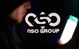 An illustrative photo of a person holding their phone with the NSO logo on a computer screen in the background, in Jerusalem, on February 7, 2022. (Yonatan Sindel/Flash90)