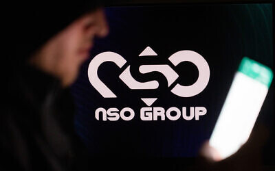 Illustrative: A man holds his phone, with the NSO Group logo in the background. (Yonatan Sindel/Flash90)