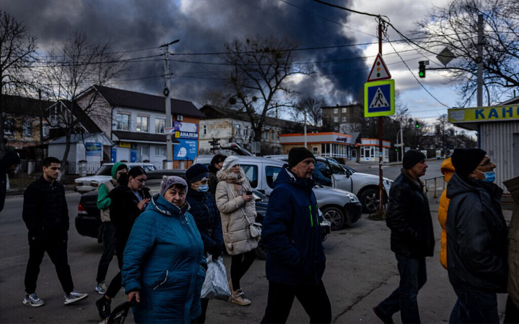 People stand in line in front of a supermarket while smoke billows over the town of Vasylkiv just outside Kyiv on February 27, 2022, after overnight Russian strikes hit an oil depot. (Dimitar Dilkoff/AFP)
