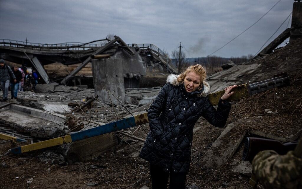A woman takes a rest after crossing a destroyed bridge as she evacuates from the city of Irpin, northwest of Kyiv, on March 7, 2022 (Dimitar DILKOFF / AFP)