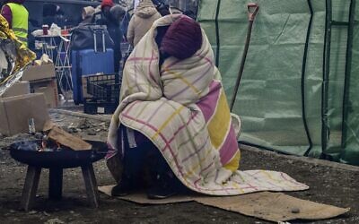 A woman tries to warm herself by a fire due to freezing cold temperatures, after crossing the Ukrainian border into Poland at the Medyka border crossing, on March 7, 2022. (Louisa Gouliamaki/AFP)