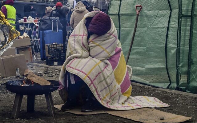 A woman tries to warm herself by a fire due to freezing cold temperatures, after crossing the Ukrainian border into Poland, at the Medyka border crossing in Poland, on March 7, 2022 (Louisa GOULIAMAKI / AFP) A woman tries to warm herself by a fire due to freezing cold temperatures, after crossing the Ukrainian border into Poland, at the Medyka border crossing in Poland, on March 7, 2022 (Louisa GOULIAMAKI / AFP)