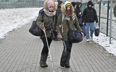 A young woman helps a visually impaired woman as they cross the border from Ukraine into Poland   at the Medyka border crossing, eastern Poland, on March 9, 2022 (Louisa GOULIAMAKI / AFP)