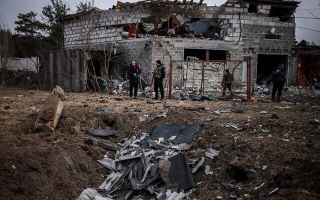 Police officers and residents stand next to a shell crater in front of a house damaged by recent shelling, on the outskirts Kyiv on March 12, 2022 (Dimitar DILKOFF / AFP)