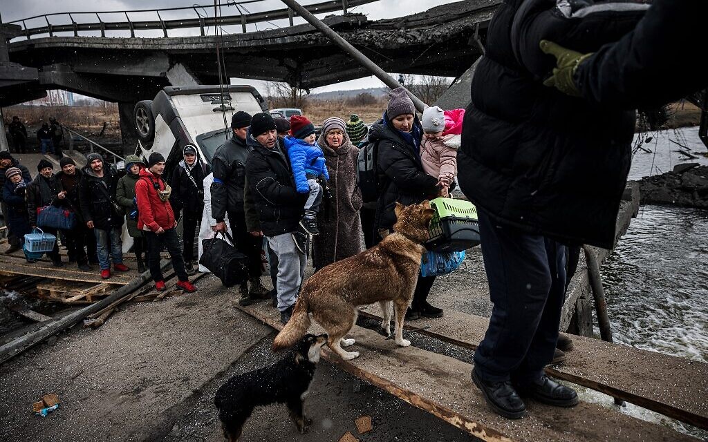 Evacuees walk on a makshift pathway to cross a river next to a destroyed bridge as they flee the city of Irpin, northwest of Kyiv, on March 13, 2022. (Dimitar Dilkoff/AFP)