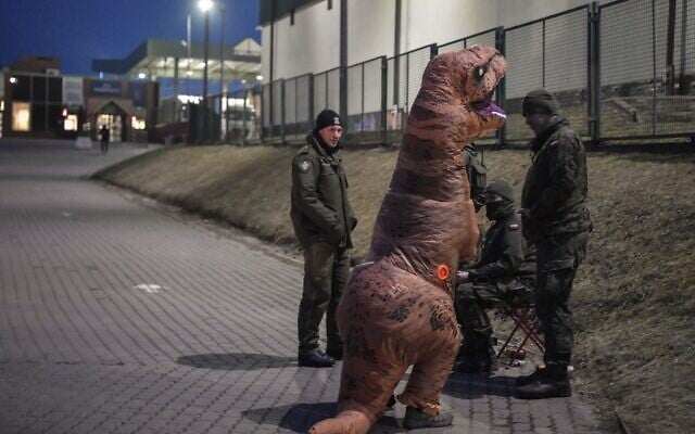 A German aid activist wearing a dinosaur costum to amuse children talks with Polish soldiers at the Medyka border crossing, southeastern Poland on March 16, 2022. (Louisa GOULIAMAKI / AFP)