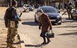 A woman crosses the street as Ukrainian servicemen stand guard at a military checkpoint in Kyiv on March 21, 2022. (Photo by FADEL SENNA / AFP)