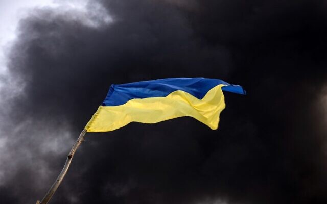 A Ukrainian national flag waves while smoke rises after Russian attacks hit a fuel storage facility in the city of Kalynivka, on March 25, 2022. (Photo by FADEL SENNA / AFP) A Ukrainian national flag waves while smoke rises after Russian attacks hit a fuel storage facility in the city of Kalynivka, on March 25, 2022. (Photo by FADEL SENNA / AFP)