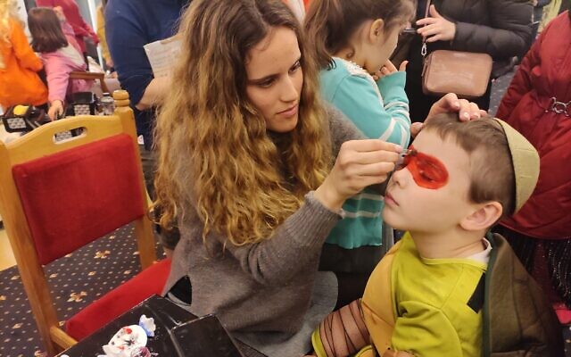 Dana Lipschitz paints a Ukrainian child’s face during Purim celebrations in Neptun, Romania, March 16, 2022. (Marcel Gascon Barbara/ JTA)