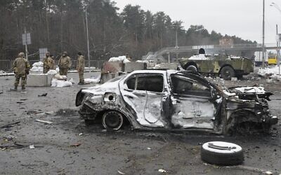 Ukrainian servicemen stand near a damaged car and an armored vehicle at a checkpoint in Brovary, outside Kyiv, Ukraine, March 1, 2022. (AP Photo/Efrem Lukatsky)